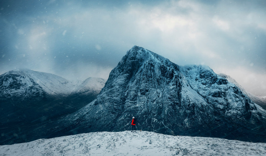 Person standing alone in front of a snow-covered mountain — the longevity journey from foundation to frontier